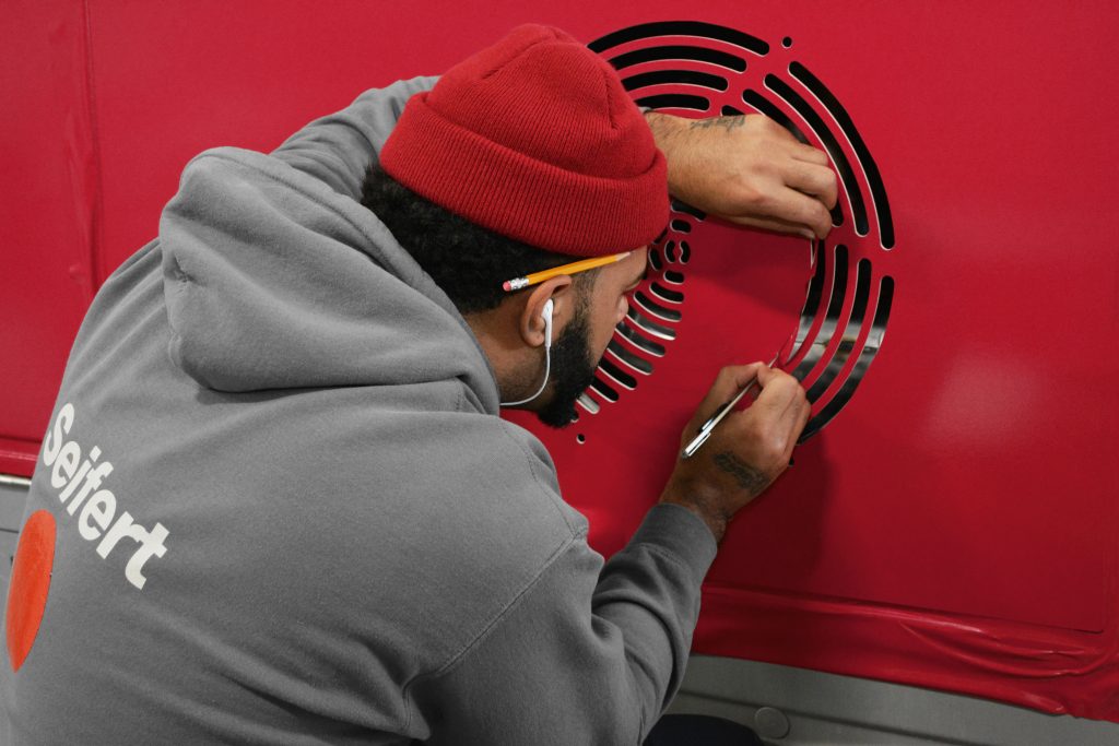 An STG team member installs vinyl intricately around a transit vehicle exhaust vent.