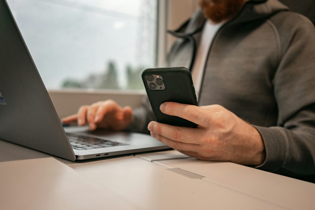 Man looking at his phone in front of a laptop